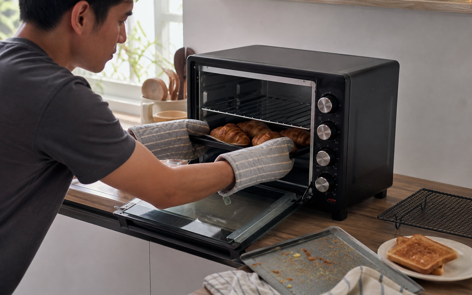 Editorial scene showing a generic countertop oven with rack, tray, open-door clearance, and nearby accessories.