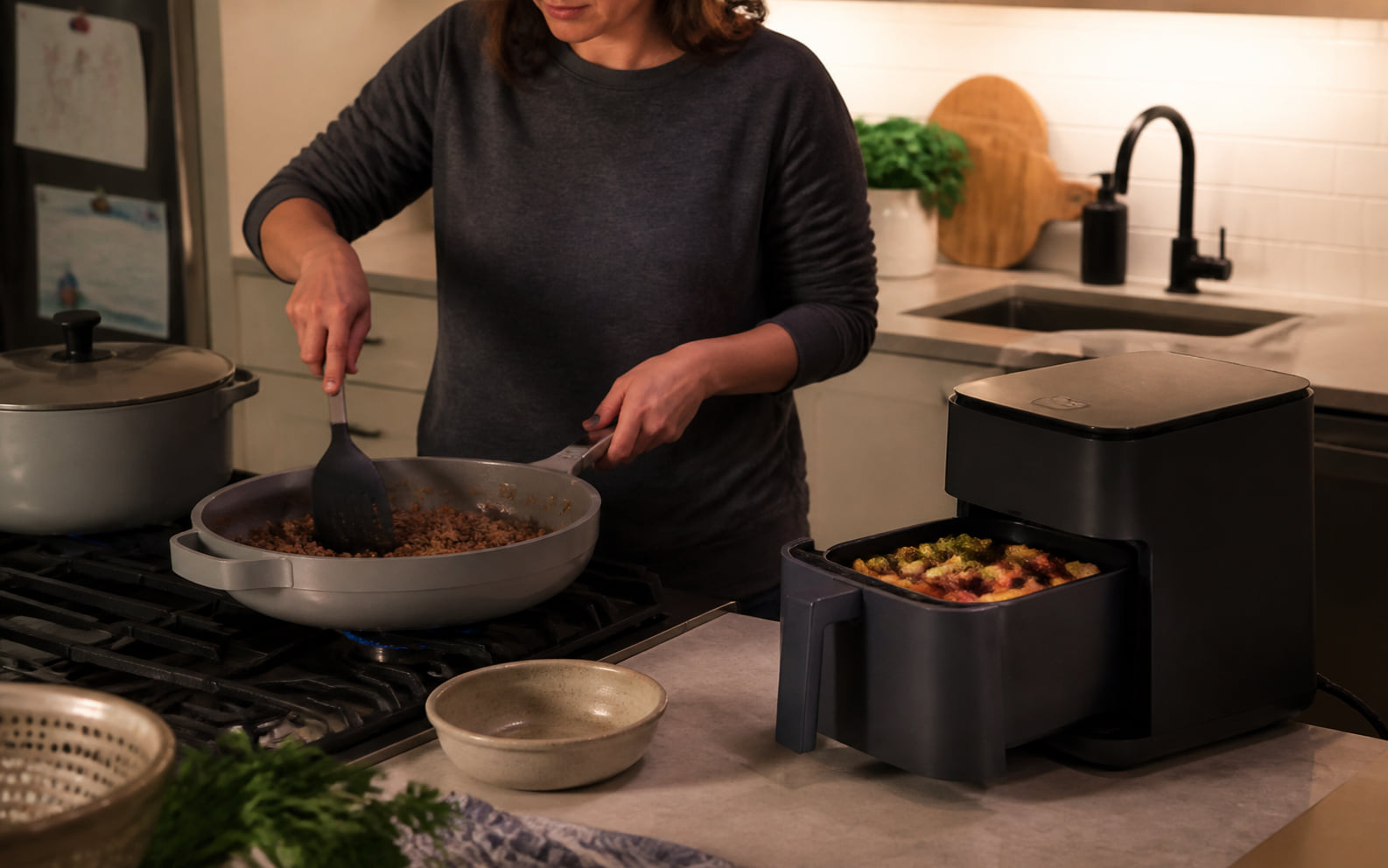 Editorial scene showing generic countertop heat taking one bounded role while the rest of dinner uses existing cookware.